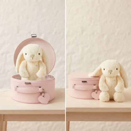 A cream-colored plush bunny stuffed animal is shown in two views beside a pink keepsake box on a light wood table against a textured off-white wall. The left view shows the case open with the bunny inside, and the right view shows the bunny sitting next to the closed case.