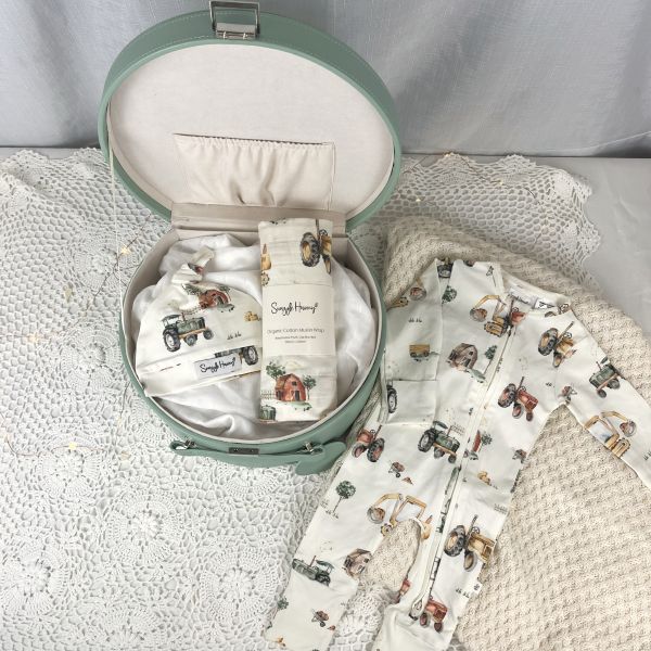 Baby wrap, beanie and romper set with digger print in a green keepsake box on a textured surface
