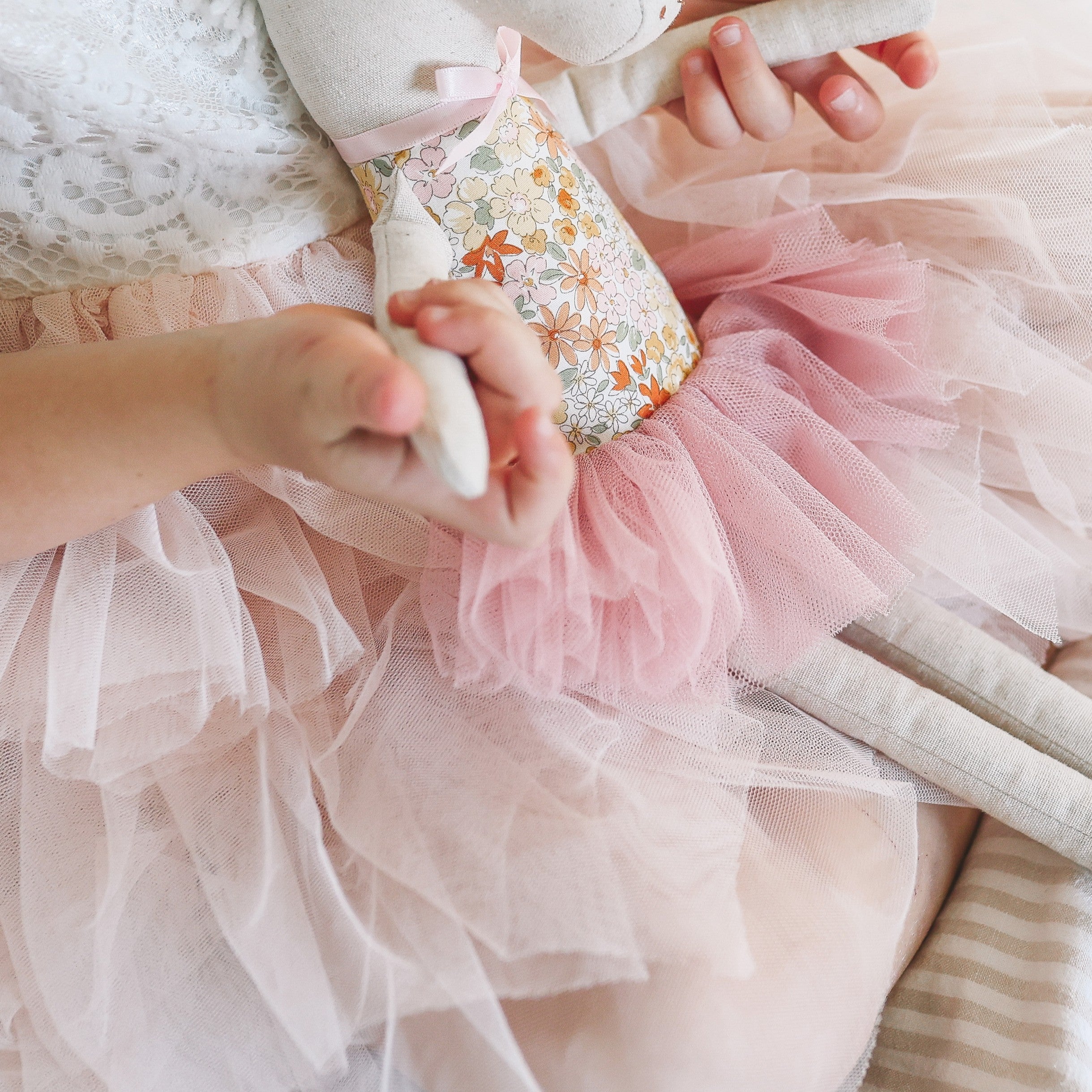 Close-up of a child's hands holding a plush toy with a floral pattern and pink tutu.