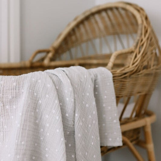 Wicker crib with a grey muslin wrap draped over it against a neutral background