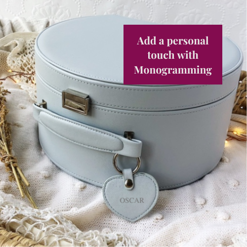 Light blue round suitcase with a heart-shaped tag on a textured surface, featuring text about monogramming.