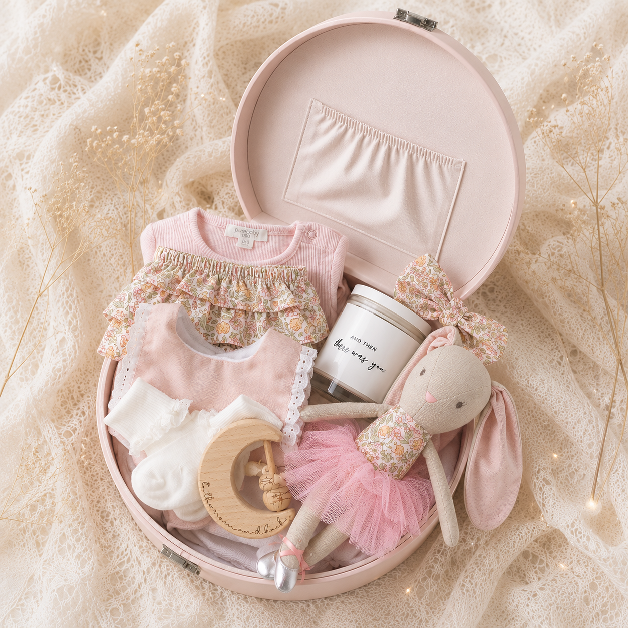 baby gift hamper with bunny toy and clothing accessories inside a pink keepsake box on neutral background