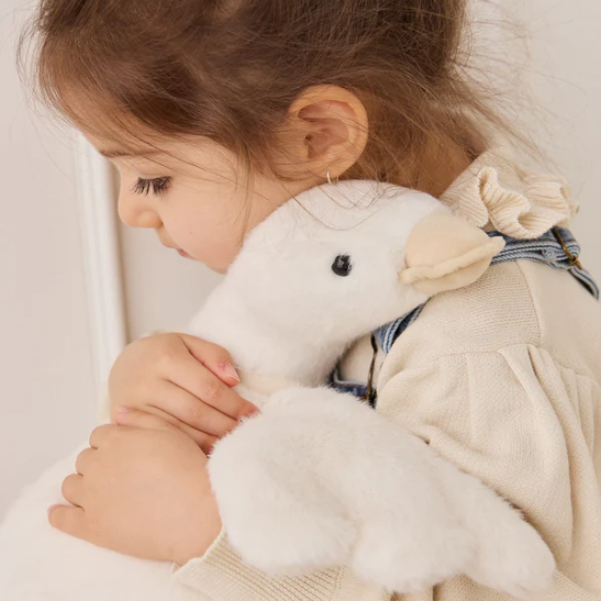 Child holding a white plush toy duck with a neutral background