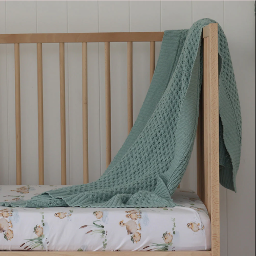 sage baby blanket draped over a timber cot