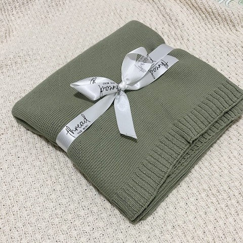 sage baby blanket on textured cream background