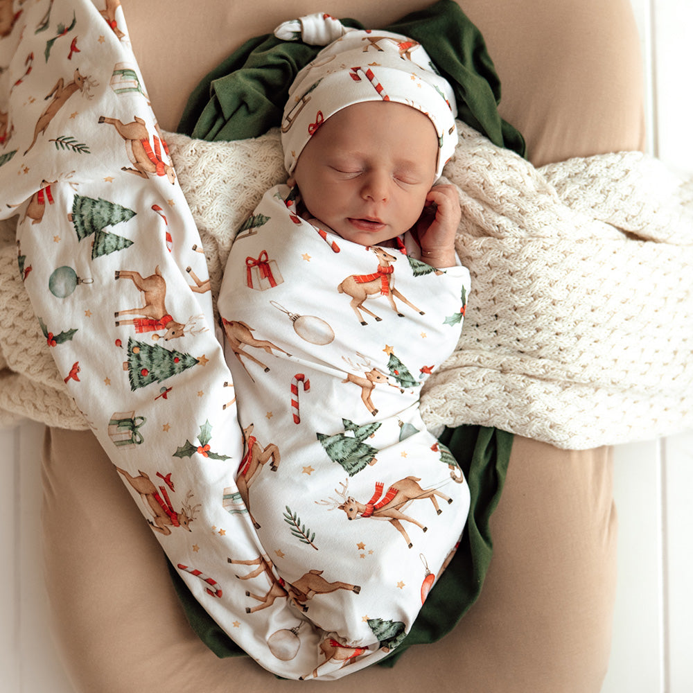 Newborn baby swaddled in a festive patterned blanket with a matching hat on a beige surface.