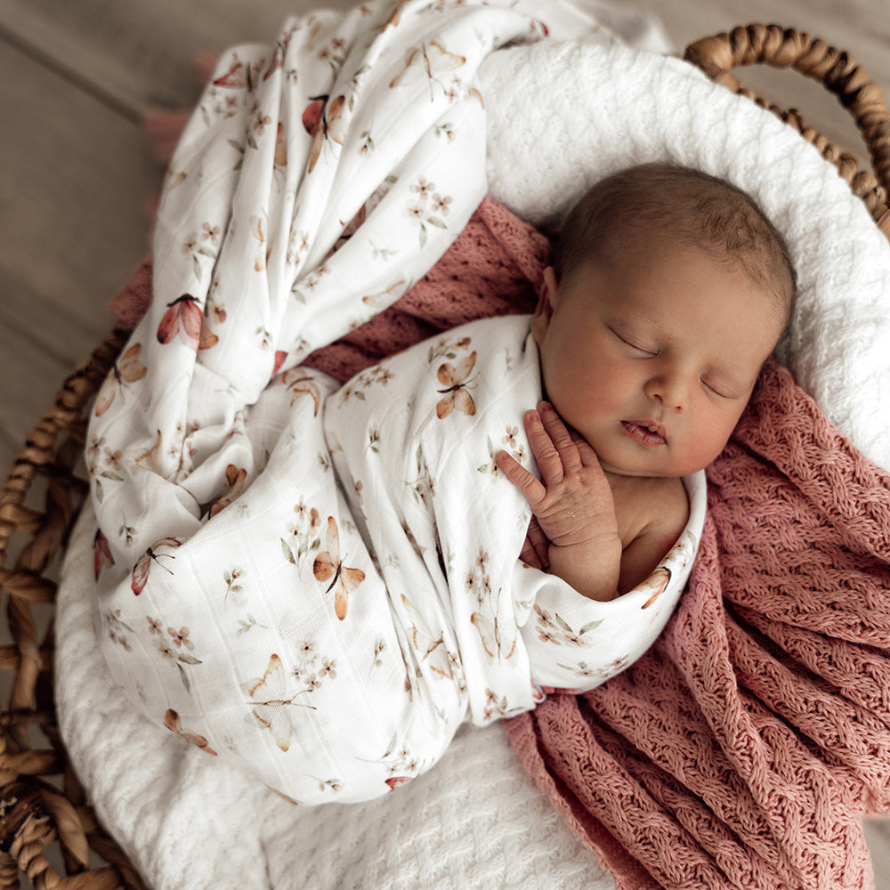 Newborn baby wrapped in a floral blanket with a pink textured blanket in a wicker basket.