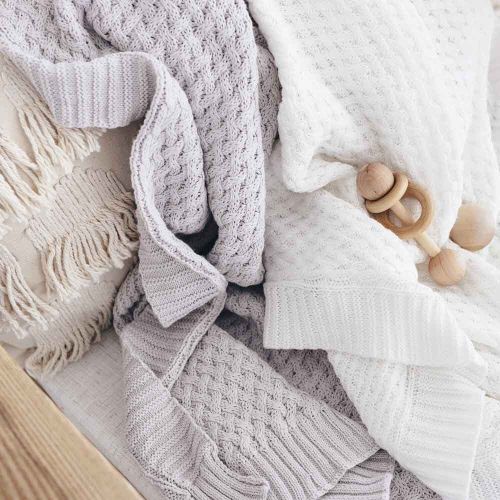 Knitted blankets and a wooden teething ring on a soft surface
