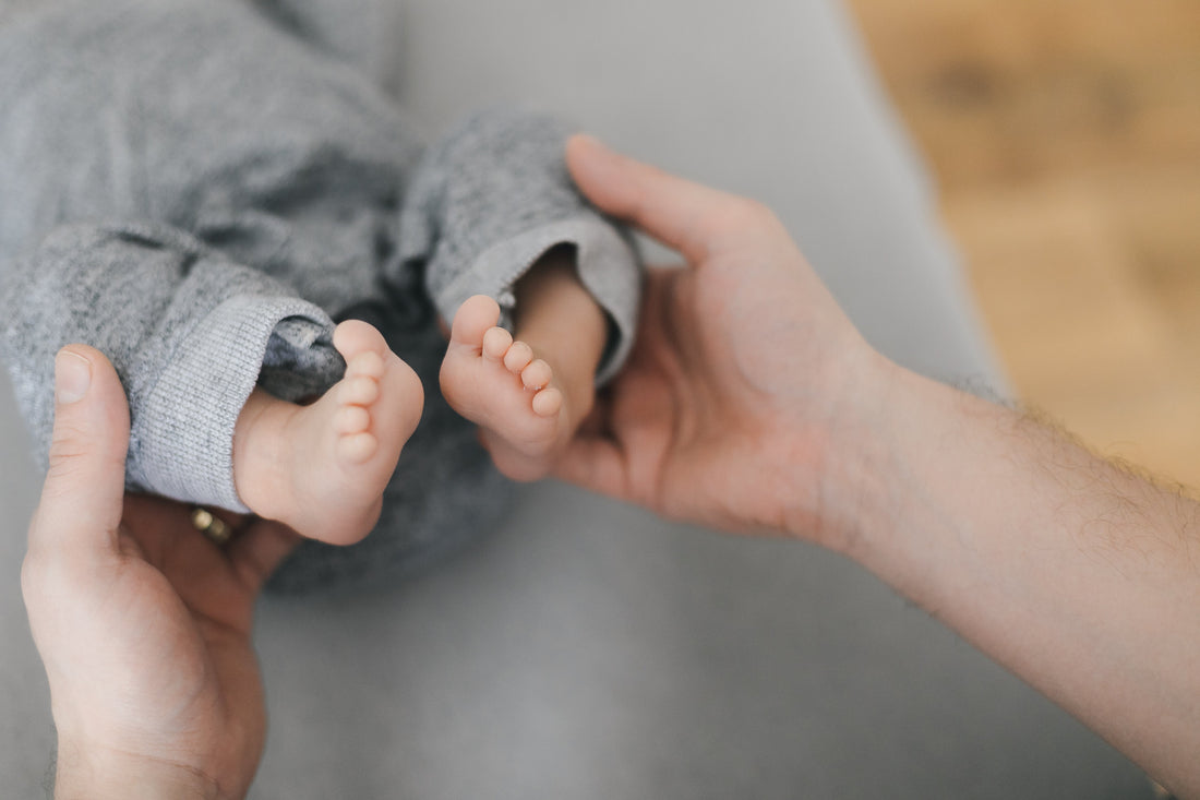 small baby dressed in grey jumpsuit with feet being cradled by an adult