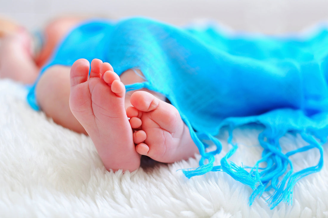 baby feet in a bed with a blue baby blanket covering the body