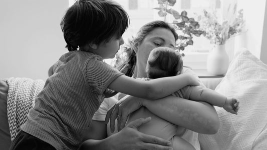 Mum sitting on a couch holding a baby with toddler cuddling from the side