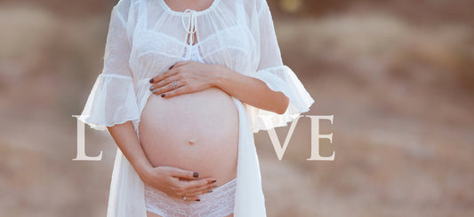 woman standing with hands around a pregnant belly dressed in a white flowing gown