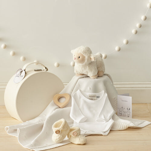 a selection of white and neutral coloured baby items including a keepsake box, baby onsie, baby booties and timber teether