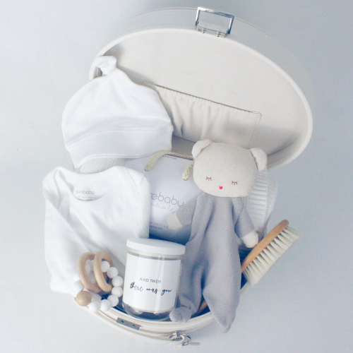 a cream keepsake box open showing comforter, baby blanket, baby clothes, baby hair brush, teether and candle inside