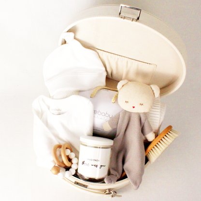 a cream keepsake box open showing comforter, baby blanket, baby clothes, baby hair brush, teether and candle inside