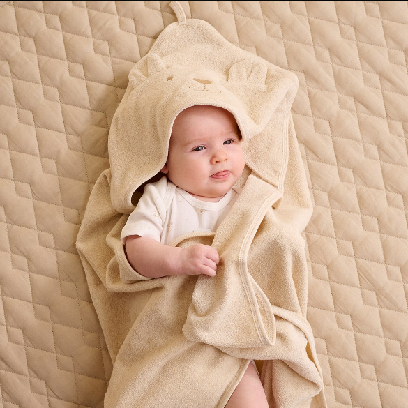 Baby wrapped in a beige towel with a hood on a quilted surface