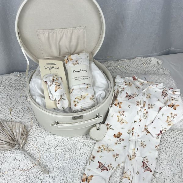 Baby items including a butterfly print outfit, swaddle, and headband in an keepsake box on a textured surface.