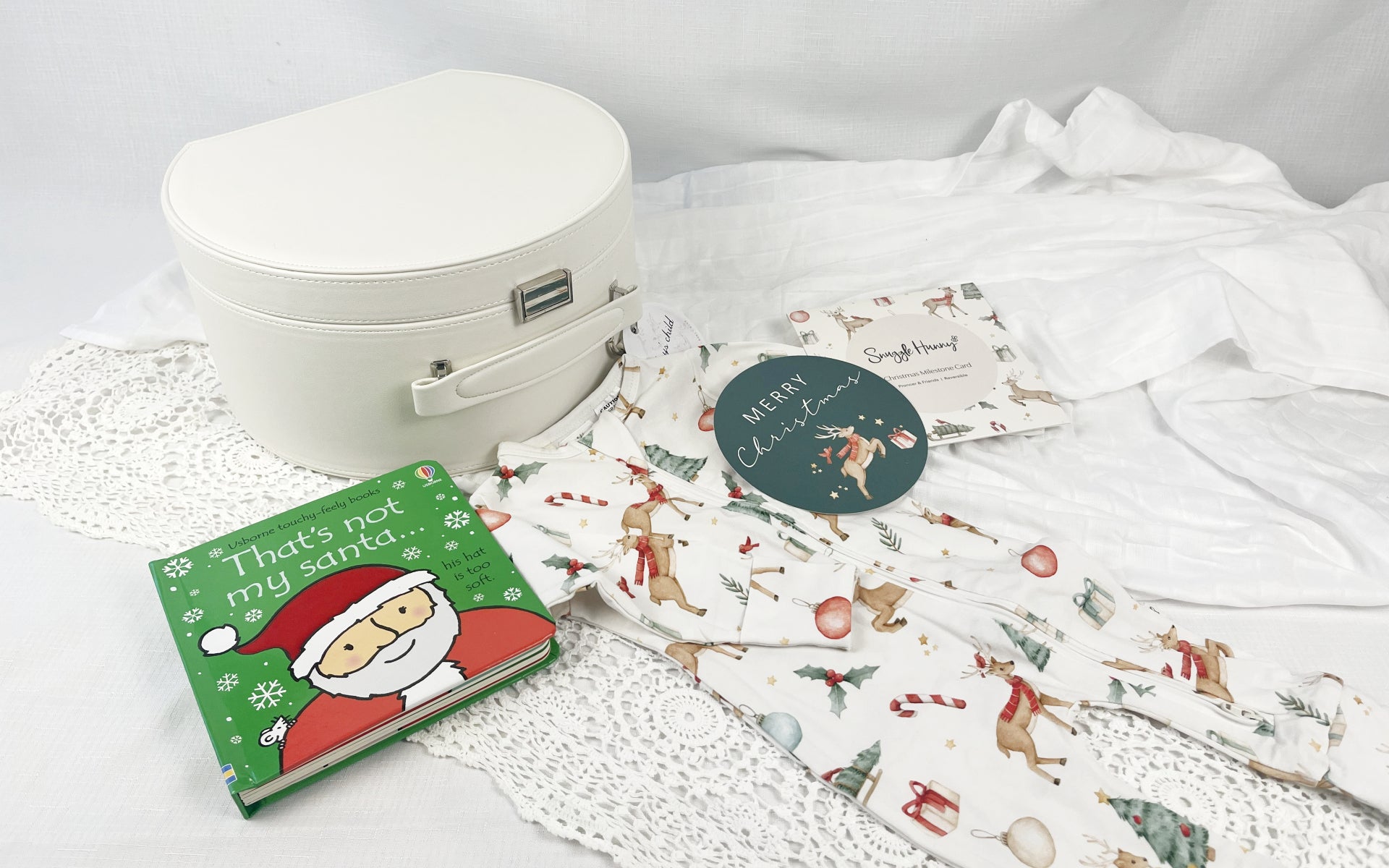 Christmas box with Christmas print baby onesie suit and milestone card laying next to it with white background