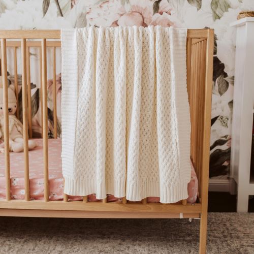 cream baby blanket draped over a timber cot