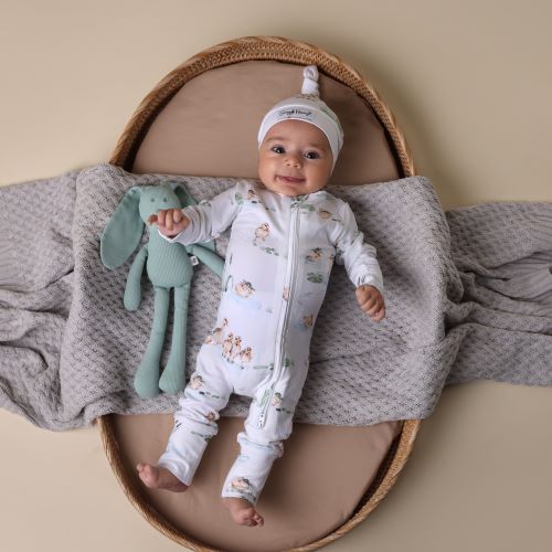 baby laying in bassinet wearing duck pond print onesie and beanie looking at camera