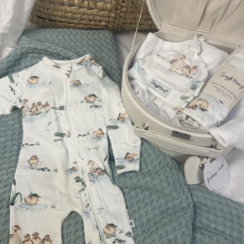 flat lay of duck pond print onesie and beanie and wrap inside cream keepsake box