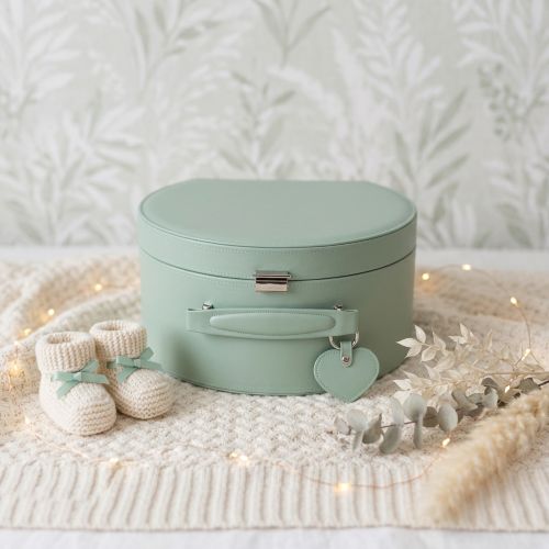 Sage green keepsake box with a heart-shaped tag on a textured surface with baby booties and decorative elements.