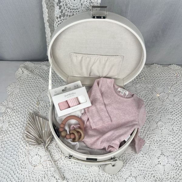 White baby keepsake box with pink baby clothes and accessories on a textured surface
