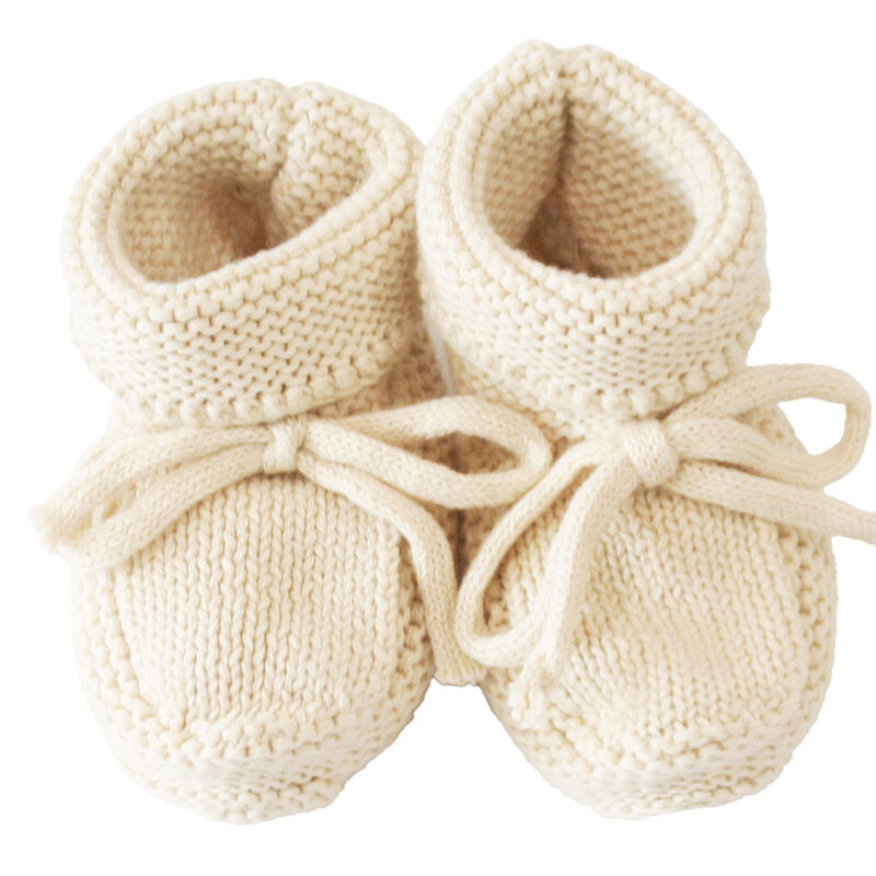 Pair of cream-colored knitted baby booties with bow details on a white background