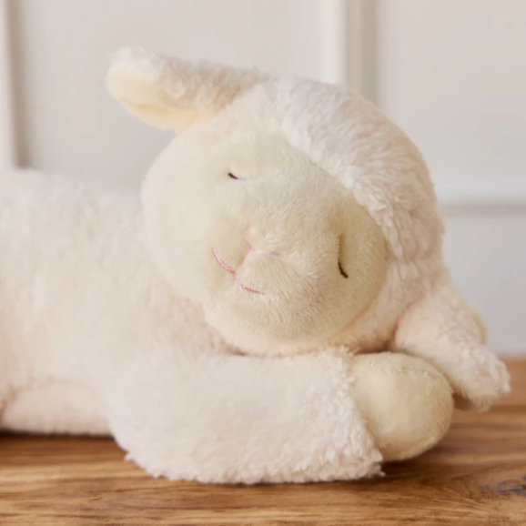 Plush lamb toy on a wooden surface with a neutral background