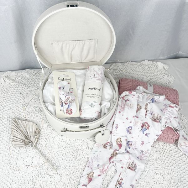 White keepsake box with baby items including a wrap, headband and romper on a textured surface.