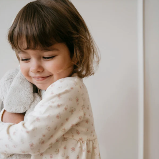 Child in a floral dress holding a plush bunny against a plain background