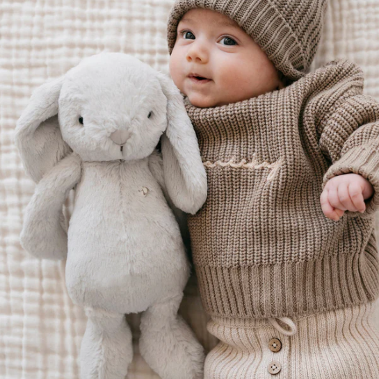 Grey plush bunny laying next to baby
