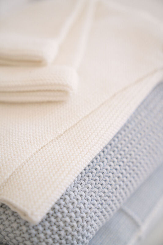 knit baby blankets folded in a stack - ivory and baby blue