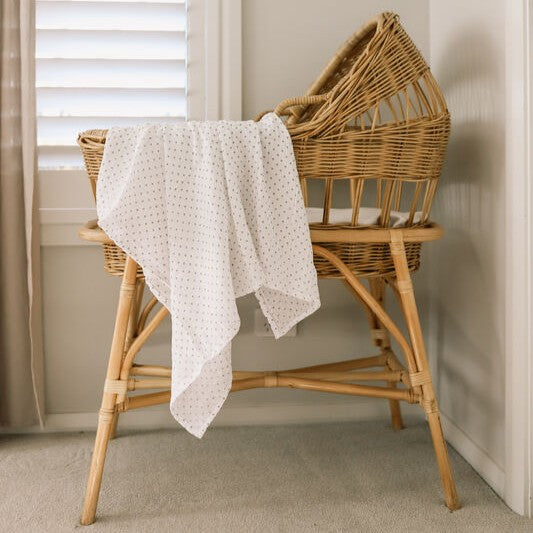 Wicker crib with a white muslin with grey spots in a neutral setting