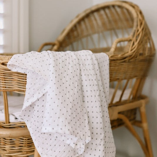 White muslin with grey spots draped over a wicker crib in a softly lit room.