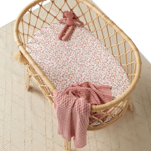 Wicker crib with floral bedding and pink blanket on a neutral background