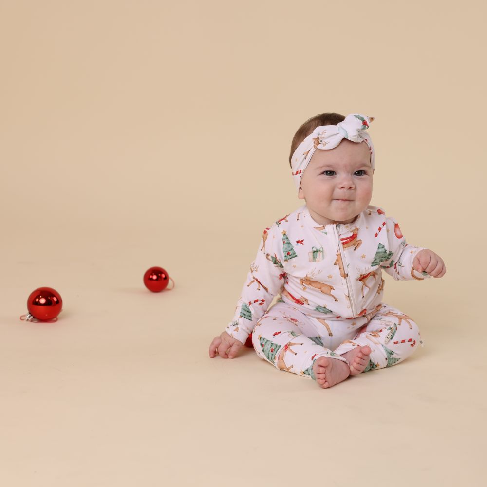 Baby in a festive outfit with Christmas-themed print on a beige background
