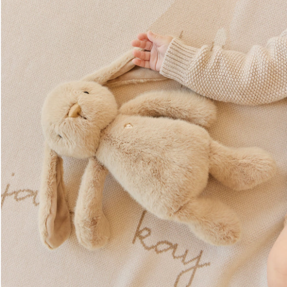 Caramel coloured bunny plush toy laying on baby blanket