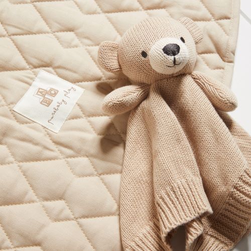 knitted bear comforter laying on a linen coloured quilted blanket