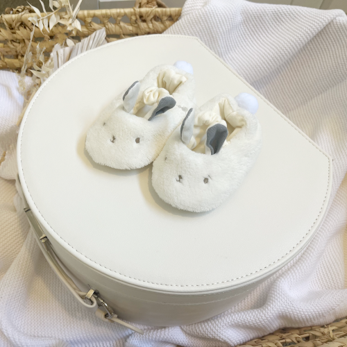 pair of fluffy white baby slippers with bunny ears on top of a cream keepsake box