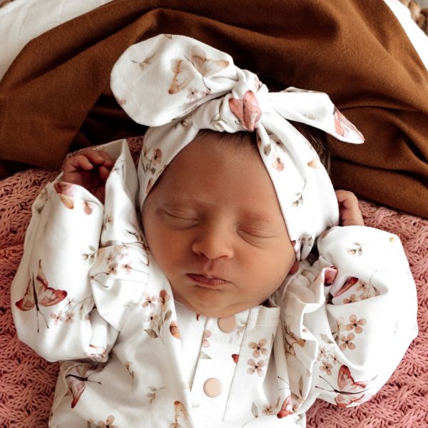 Newborn baby wearing a butterfly print headband and wrap on a brown blanket