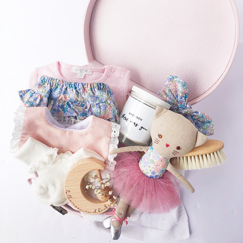 baby girl gift hamper in a pink keepsake box with various pink and floral clothing pieces, a baby hair brush, a candle, a ballerina doll and baby teether