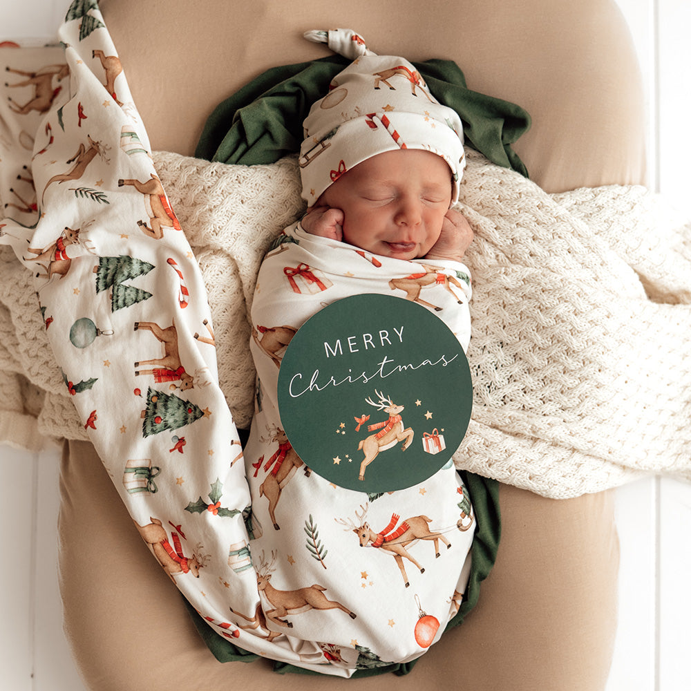 Newborn baby wrapped in a Christmas-themed blanket with a 'Merry Christmas' sign.