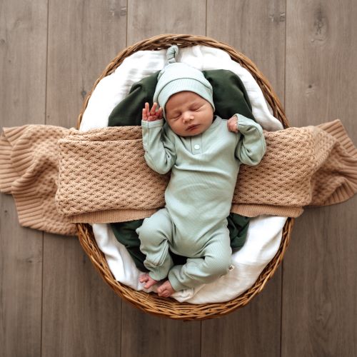 sleeping baby in bassinet wearing a sage onesie and knotted beanie