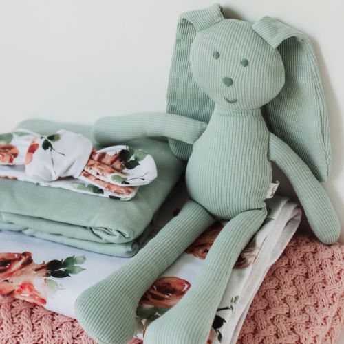 sage snuggle bunny toy sitting next to a pile of folded baby bedding