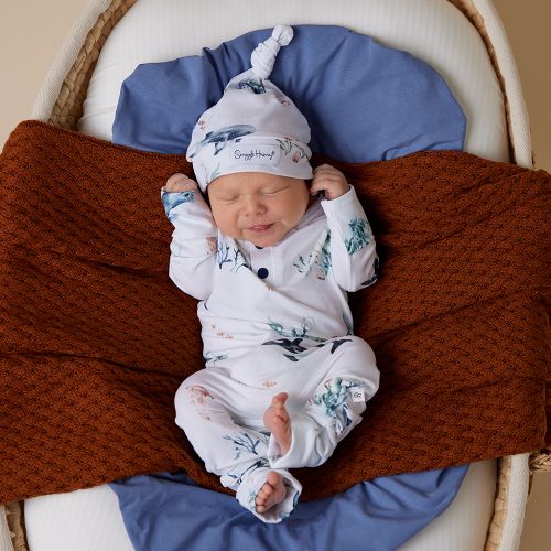 sleeping baby dressed in white and blue ocean onesie and knotted beanie