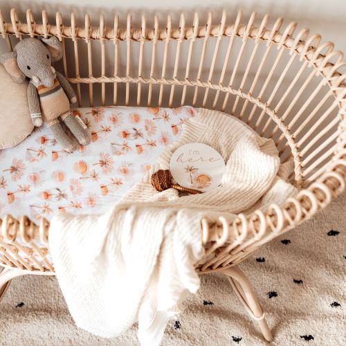 Baby crib with floral bedding, plush toy, and 'I'm here' sign on a neutral background
