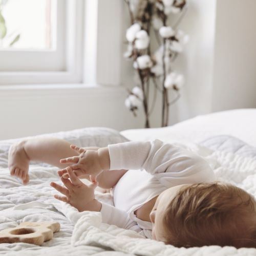 baby in white body suit rolling over on bed with white duvet